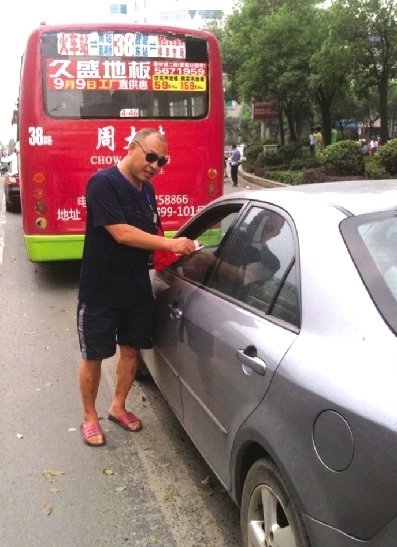 8月17日，邵陽(yáng)市西湖路與寶慶路交接處，穿拖鞋戴墨鏡的市容監(jiān)督員在對(duì)占?jí)喊唏R線停放的車輛罰款。圖/記者龍?jiān)? hspace=